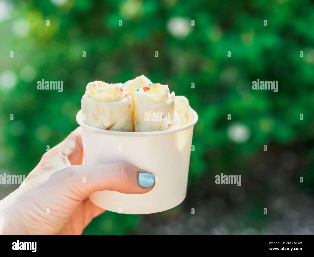Hand hält gerolltes Eis in Konusbecher Stockfoto