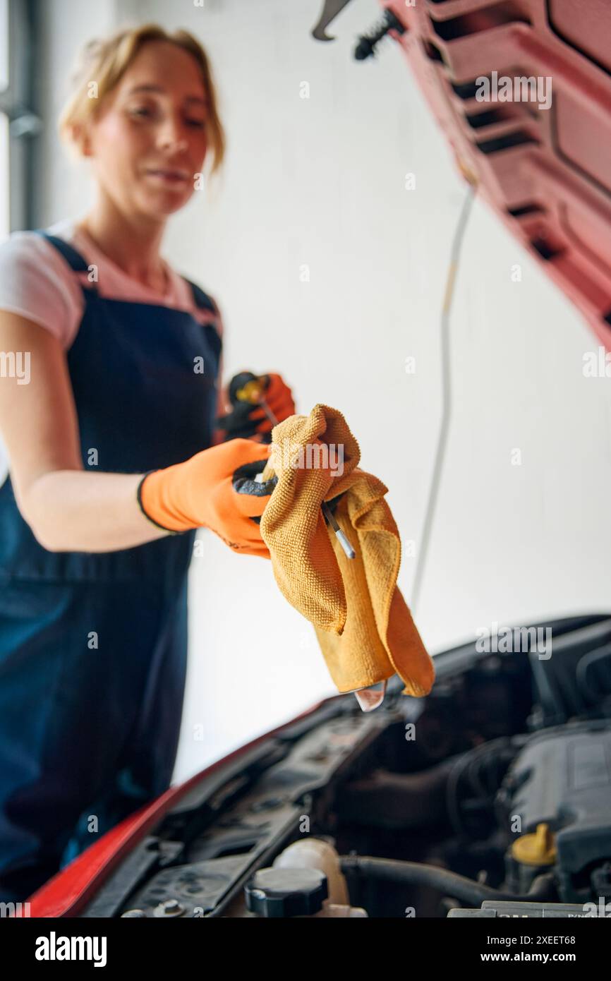 Weibliche Automechanikerin, Die Unter Der Motorhaube Des Fahrzeugs Nachsieht Und Den Ölstand Mit Dem Messstab Überprüft Stockfoto