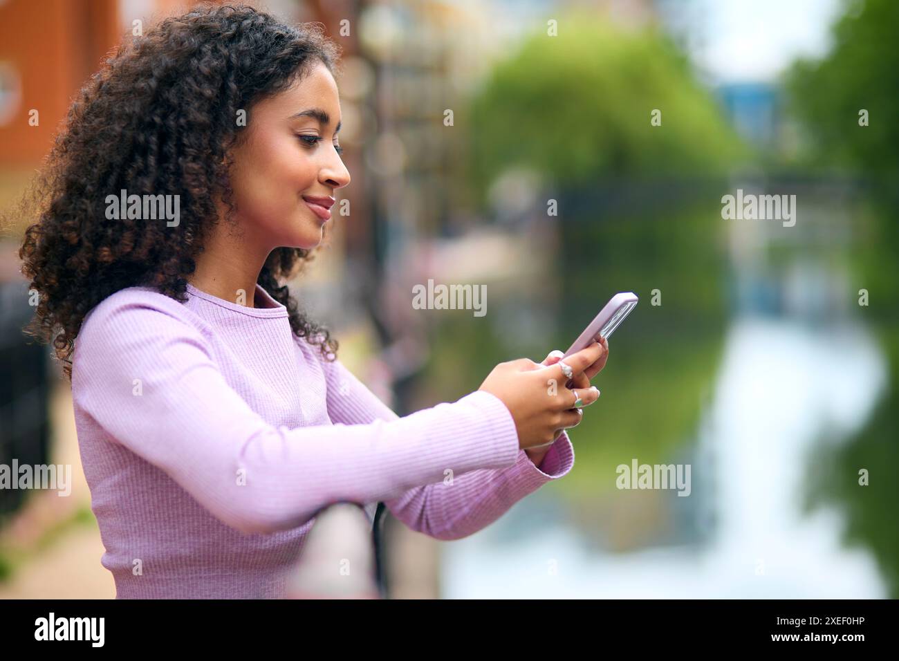 Junge Frau, Die Am Fluss Steht, In Stadtgebieten Mit Handy Für Nachrichten Oder Soziale Medien Stockfoto