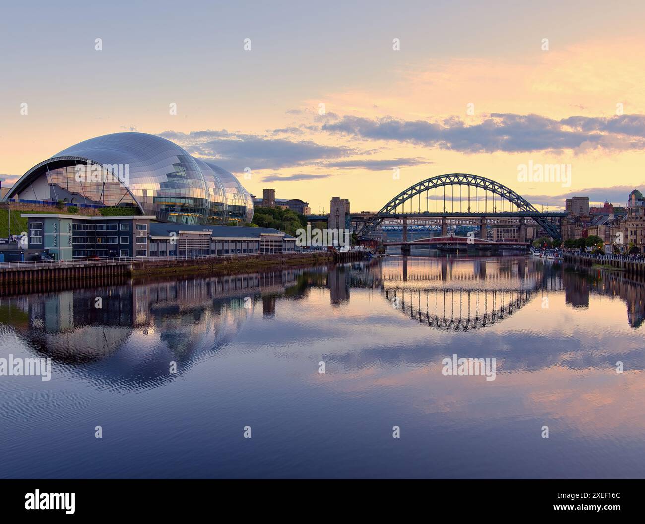 Die Tyne Bridge bildet sich vor einem Sonnenuntergang, während das Glasshouse die pastellfarbenen Farben reflektiert, die sich alle im Fluss Tyne widerspiegeln. Stockfoto