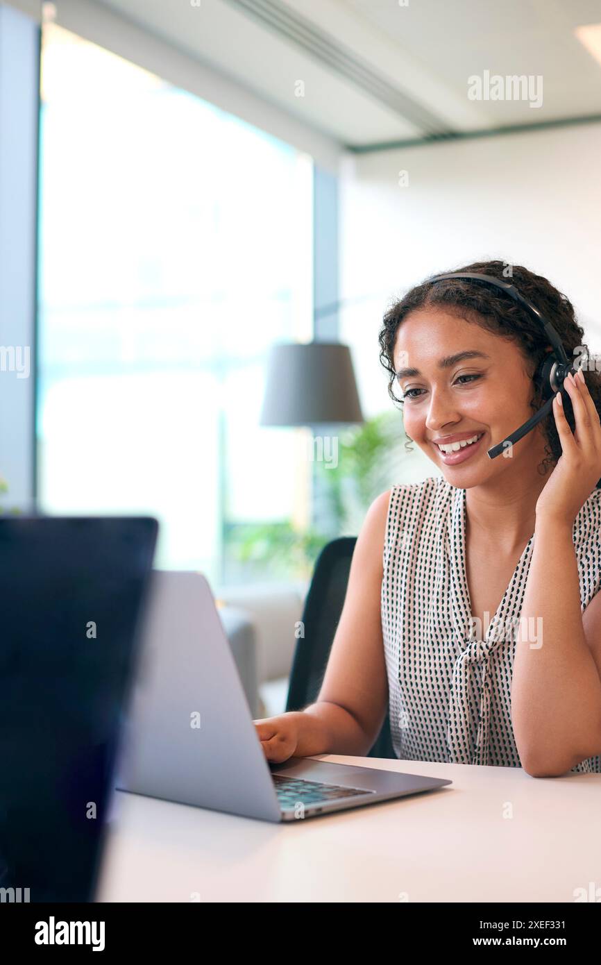Frau Mit Headset Am Schreibtisch Mit Laptop Im Büro Callcenter-Team, Das Anrufe Entgegennimmt Stockfoto