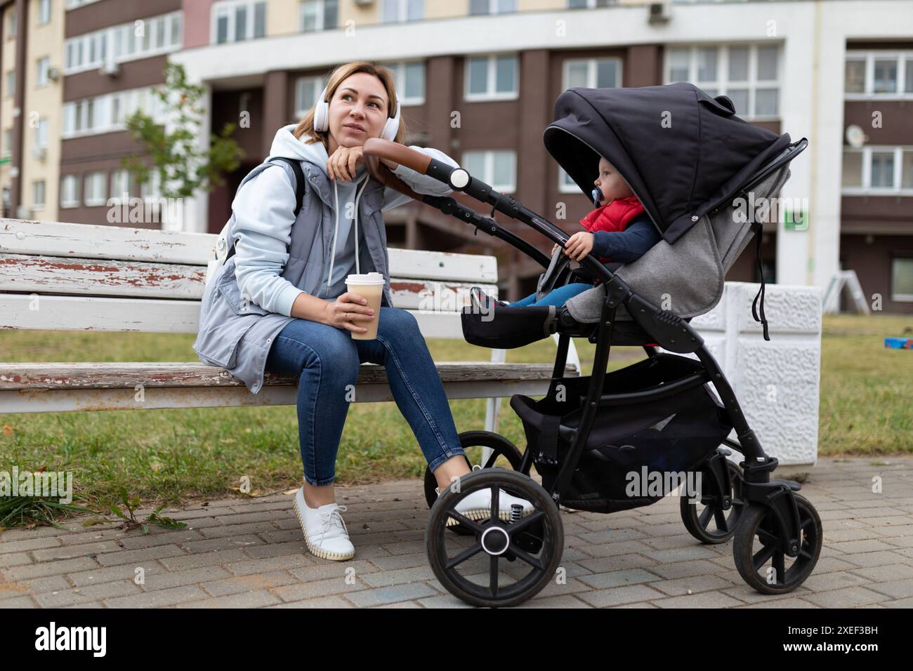 Glückliche junge Frau Eltern mit ihrem kleinen Sohn in einem Kinderwagen spazieren durch den Park und entspannen sich bei Kaffee Stockfoto