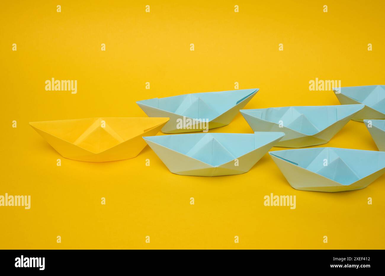 Eine Gruppe blauer Papierboote folgt gelb auf gelbem Hintergrund. Starkes Führungskonzept, Massenmanipulation. Starten einer Busine Stockfoto