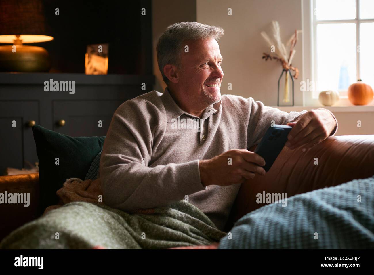 Reifer Mann Zu Hause Sitzt Auf Sofa Mit Warmer Decke Streaming Auf Handy Stockfoto