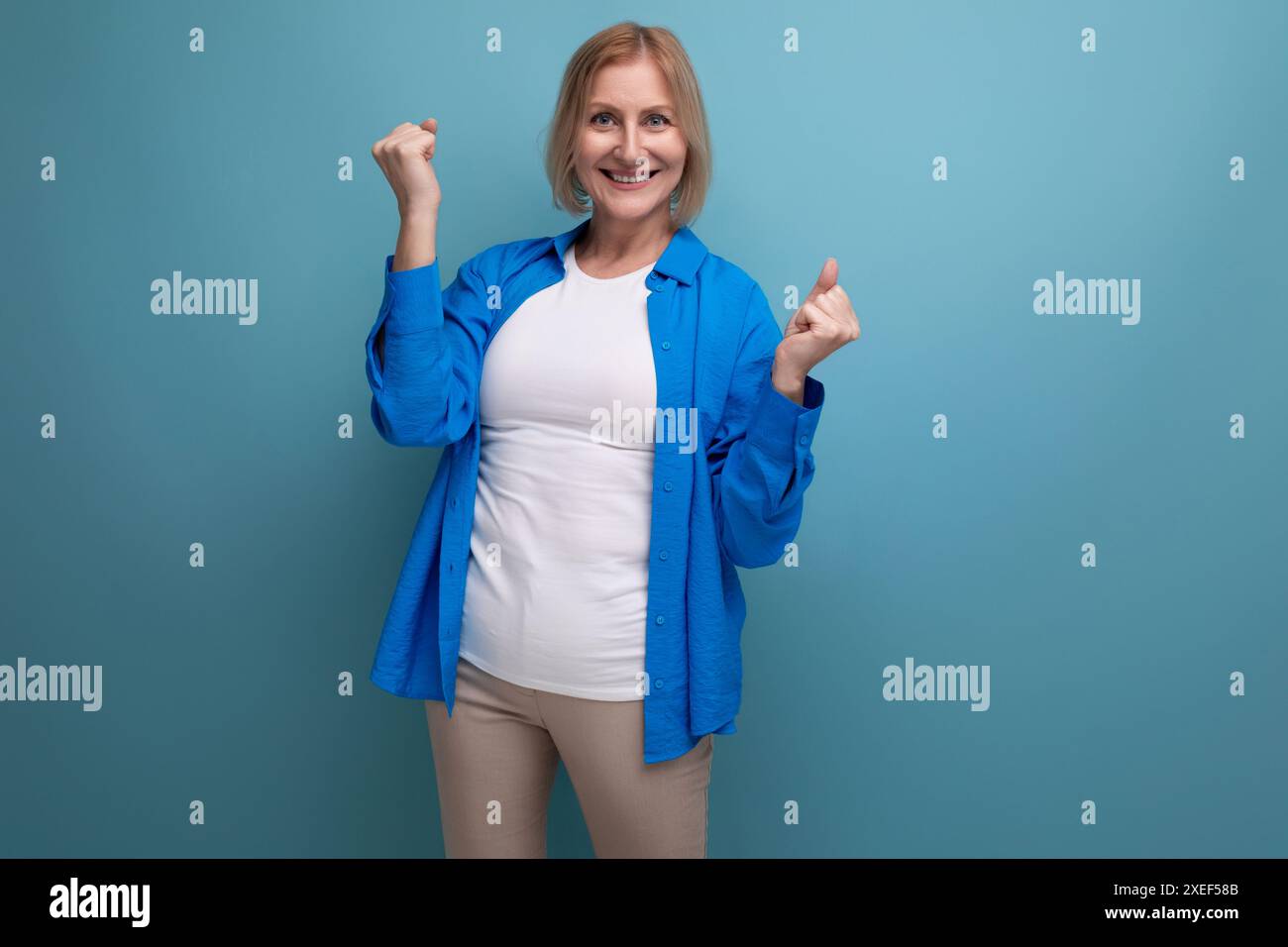 Porträt der positiven blonden 60er Jahre Frau in blauem stilvollem Hemd auf Studiohintergrund Stockfoto