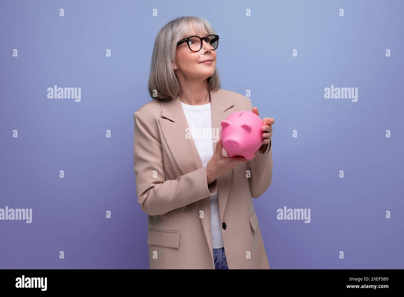 Niedliche alte Frau in einer Jacke mit einer Sparkasse auf einem hellen Hintergrund mit Kopierraum Stockfoto