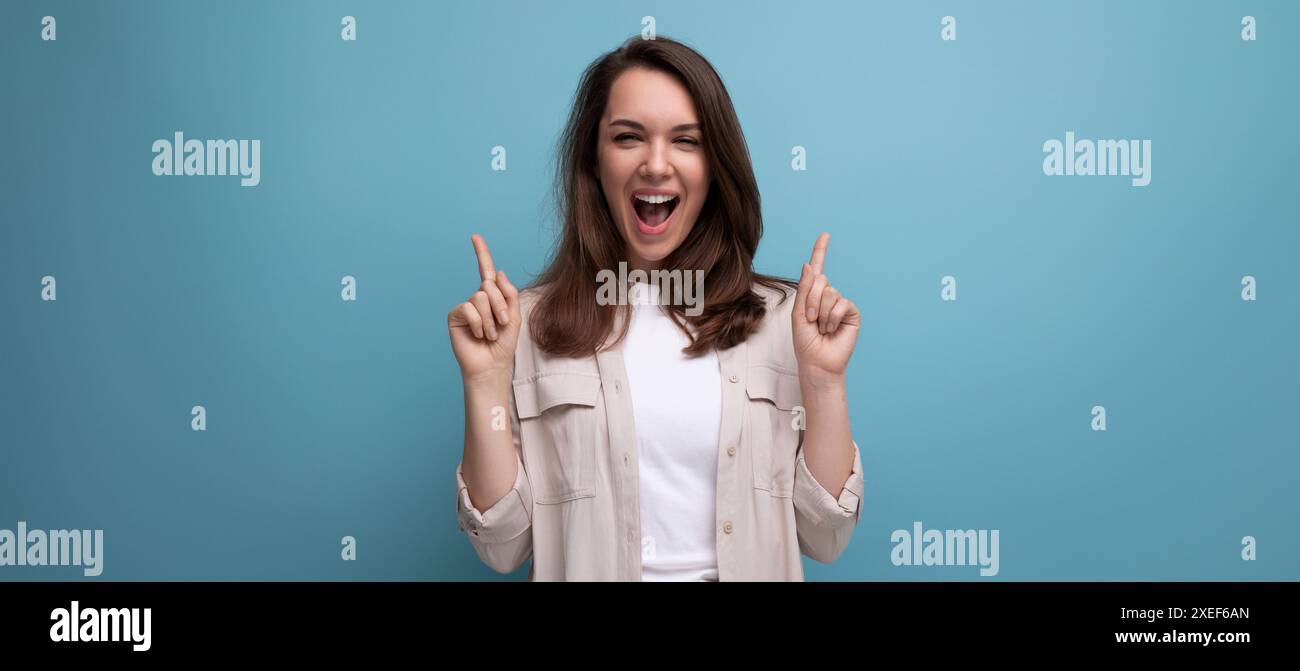 Ekstatische 30er Jahre dunkelhaarige Frau in beigem Hemd auf blauem Hintergrund Stockfoto