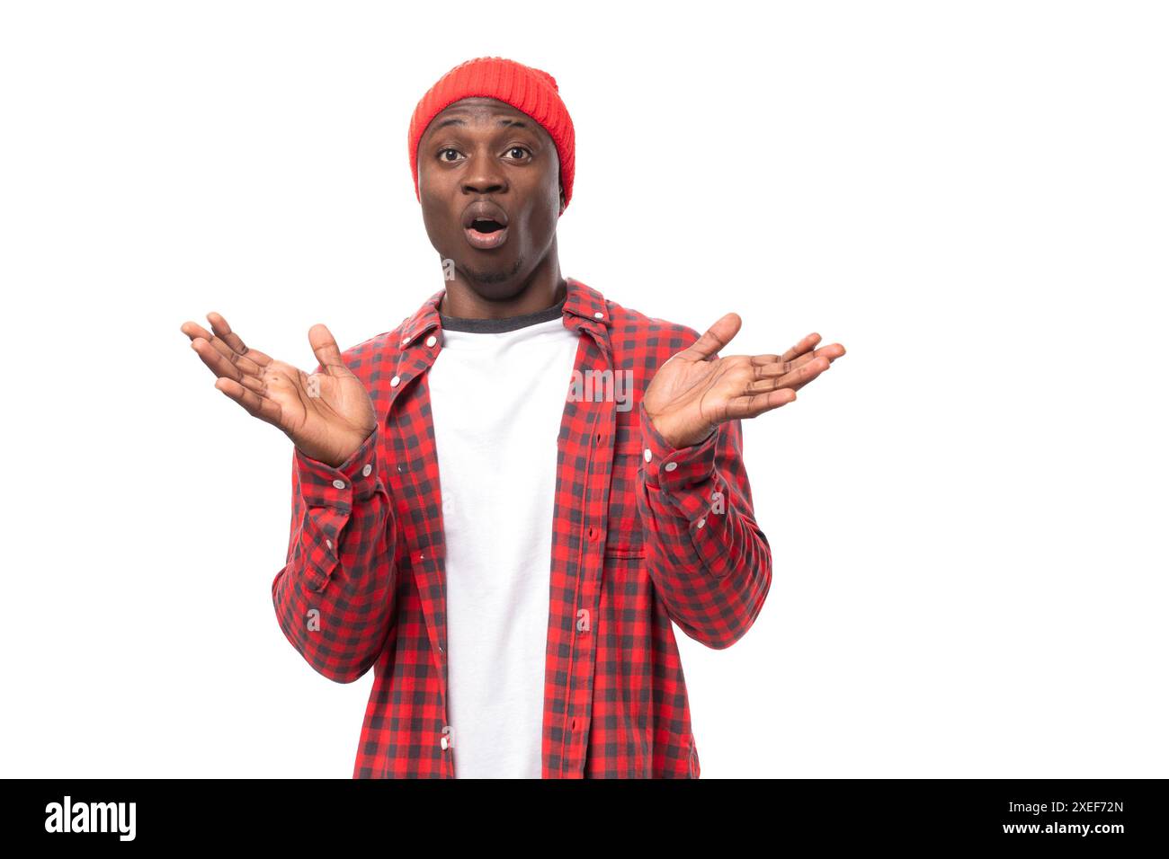 Überraschter positiver junger afrikanischer Mann in Mütze und Hemd, der Nachrichten auf isoliertem weißem Hintergrund erzählt Stockfoto
