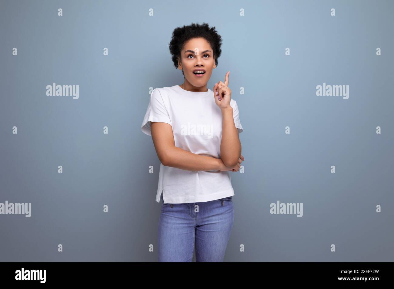 Eine junge brünette Frau mit Afro-Haaren in einem weißen T-Shirt demonstriert mit Inspiration mit Hilfe ihrer Hände eine Werbung Stockfoto