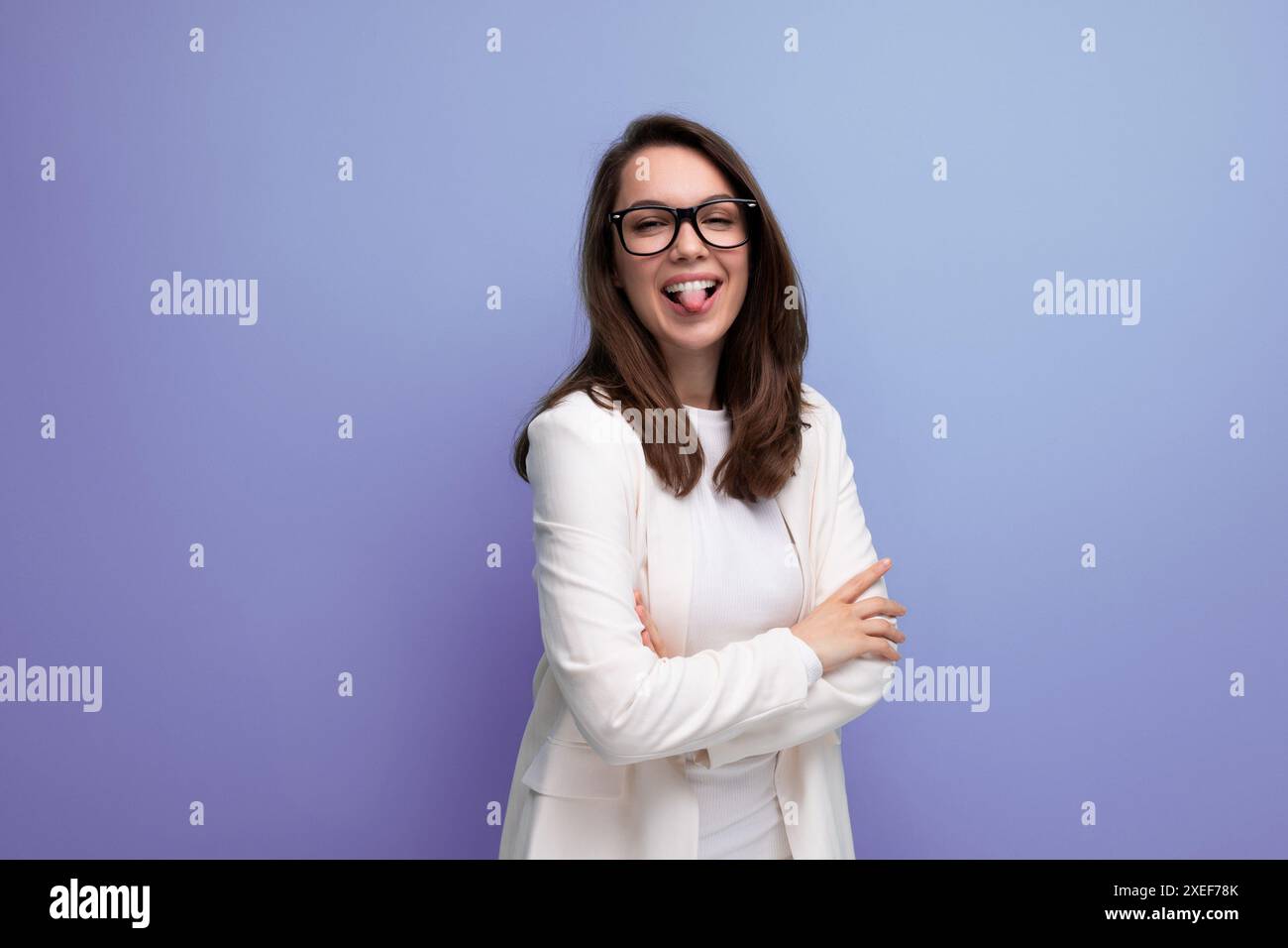 Positive junge Brünette Frau im weißen Bürokleid auf blauem Atelierhintergrund Stockfoto