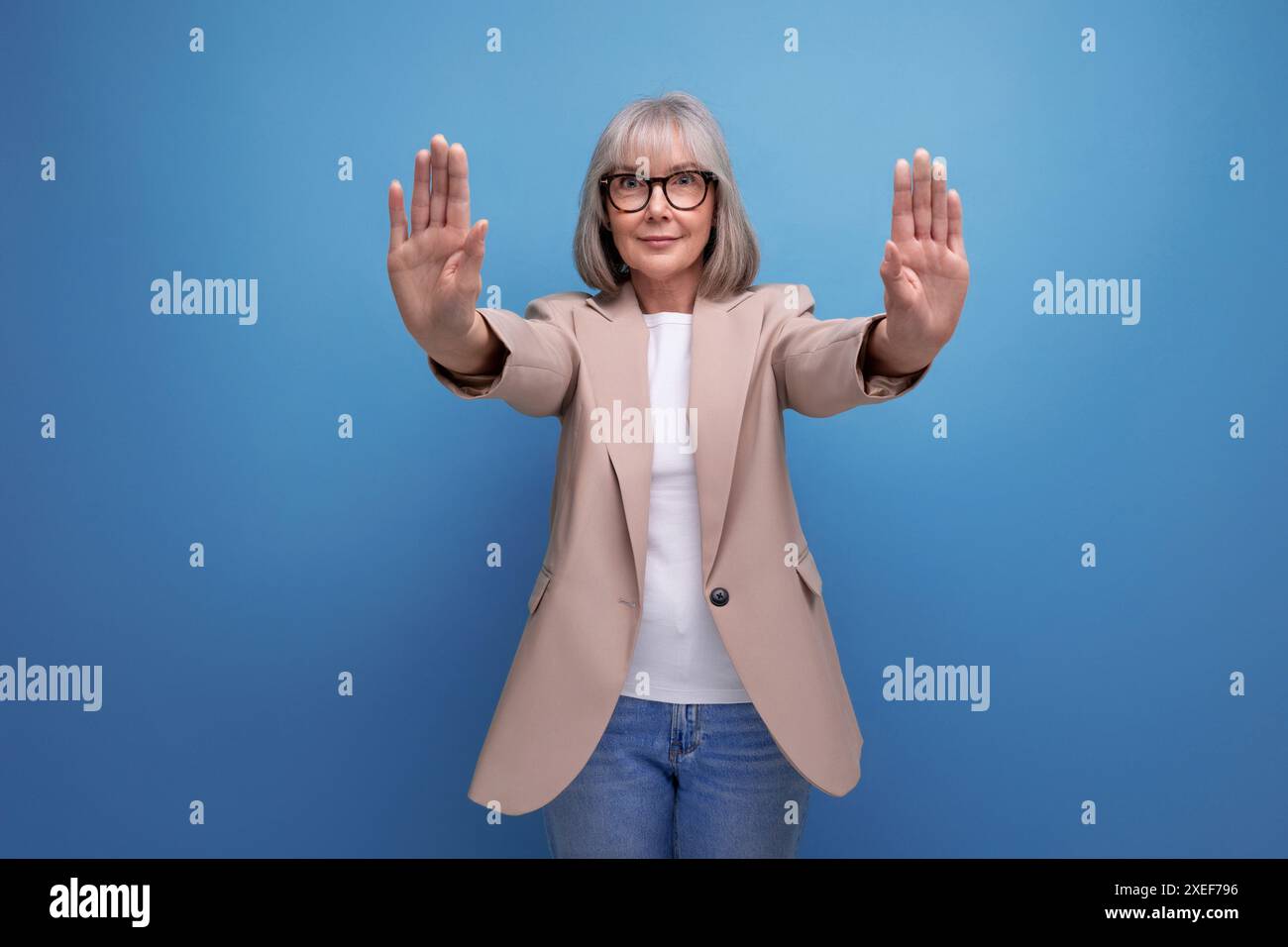 Eine stilvolle, reife alte Frau in einer Jacke lehnt etwas auf einem hellen Hintergrund mit Kopierraum ab Stockfoto