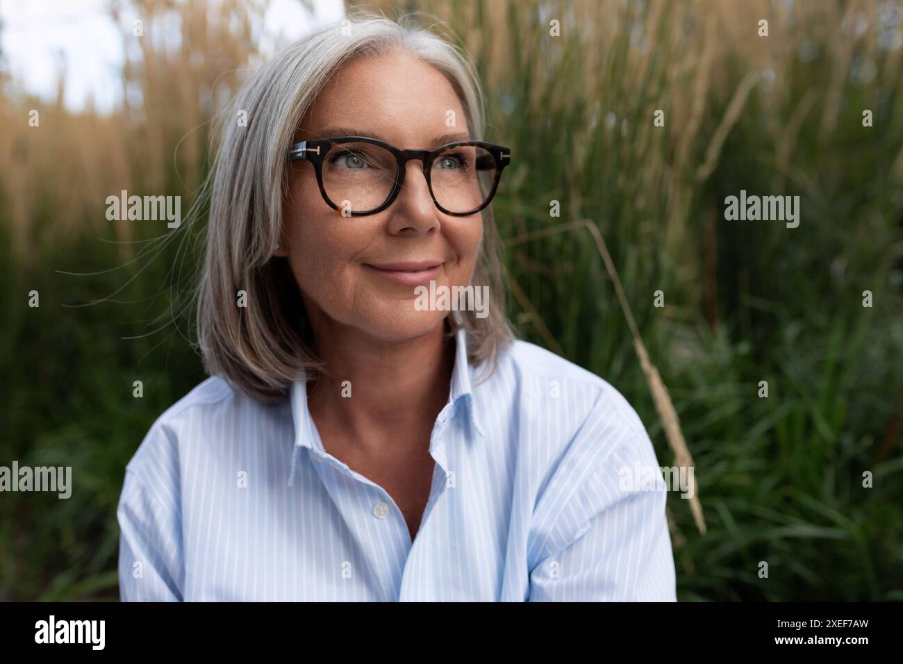 Eine schlanke, süße, grauhaarige Geschäftsfrau, weiße Frau reifer Jahre in einem hellen Hemd, geht auf die Straße Stockfoto