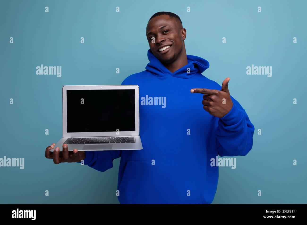 Hübscher afrikanischer junger Berater in stilvollem Hoodie mit Laptop, um Werbeanzeigen im Hintergrund mit Kopierraum zu zeigen Stockfoto
