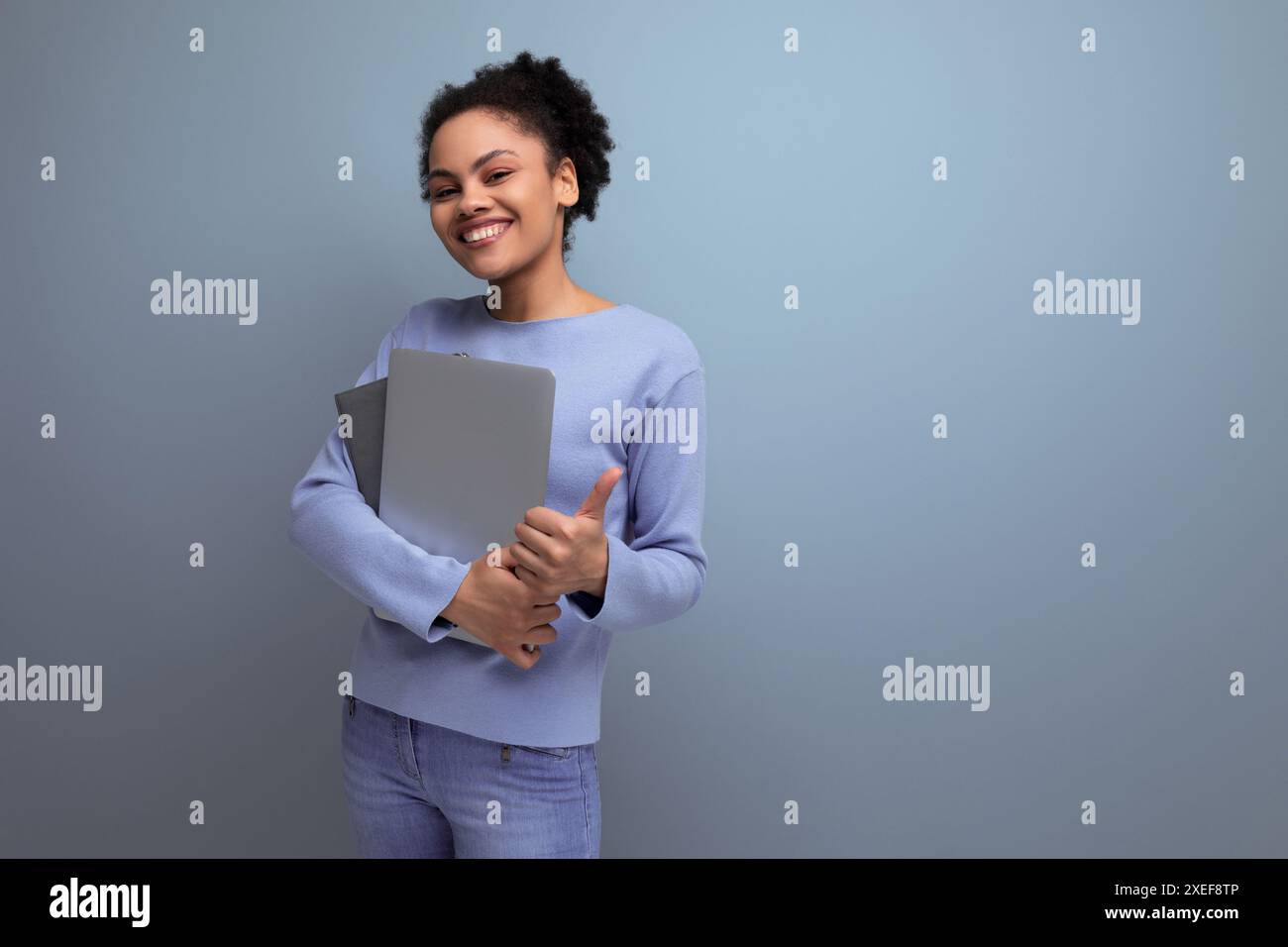 Erfolgreiche junge afro-brünette Studentin mit Laptop und Dokumenten in der Hand Stockfoto