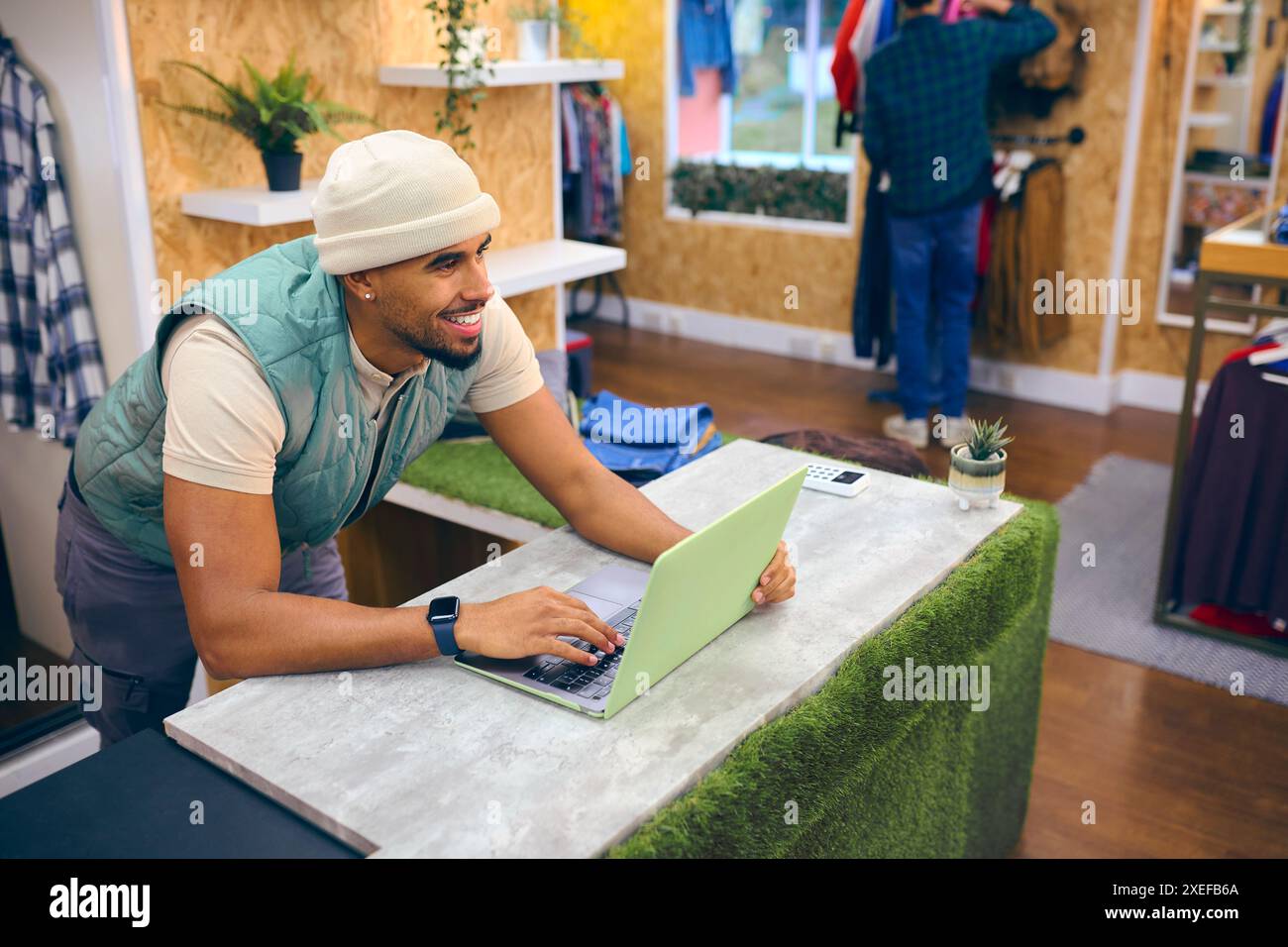 Männlicher Verkaufsassistent An Der Kasse Im Pop-Up-Mode- Oder Kleiderladen Mit Laptop Stockfoto