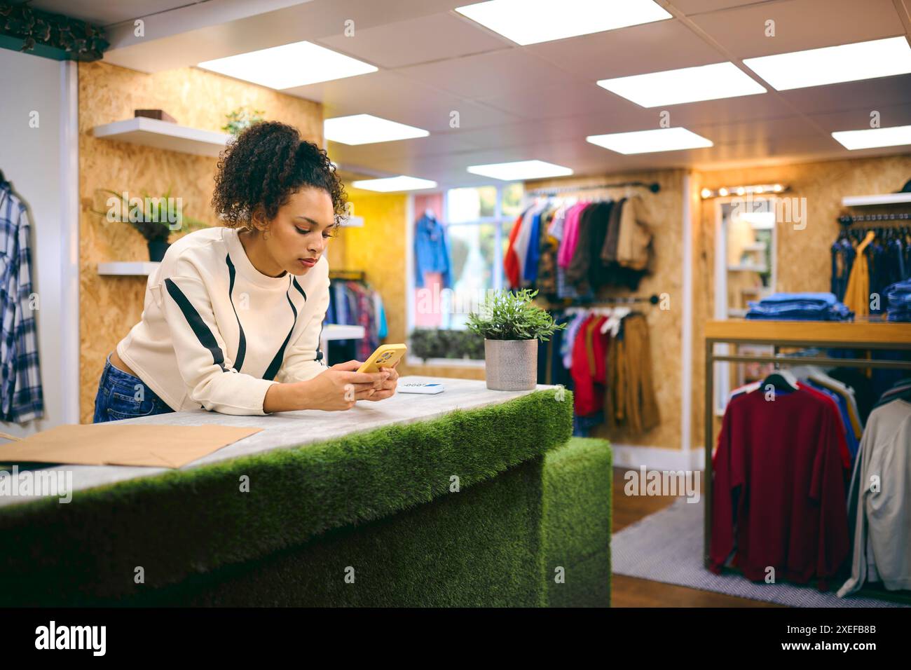 Weibliche Verkäuferin An Der Kasse Im Pop-Up-Mode- Oder Kleidergeschäft, Die Sich Ein Mobiltelefon Anschaut Stockfoto
