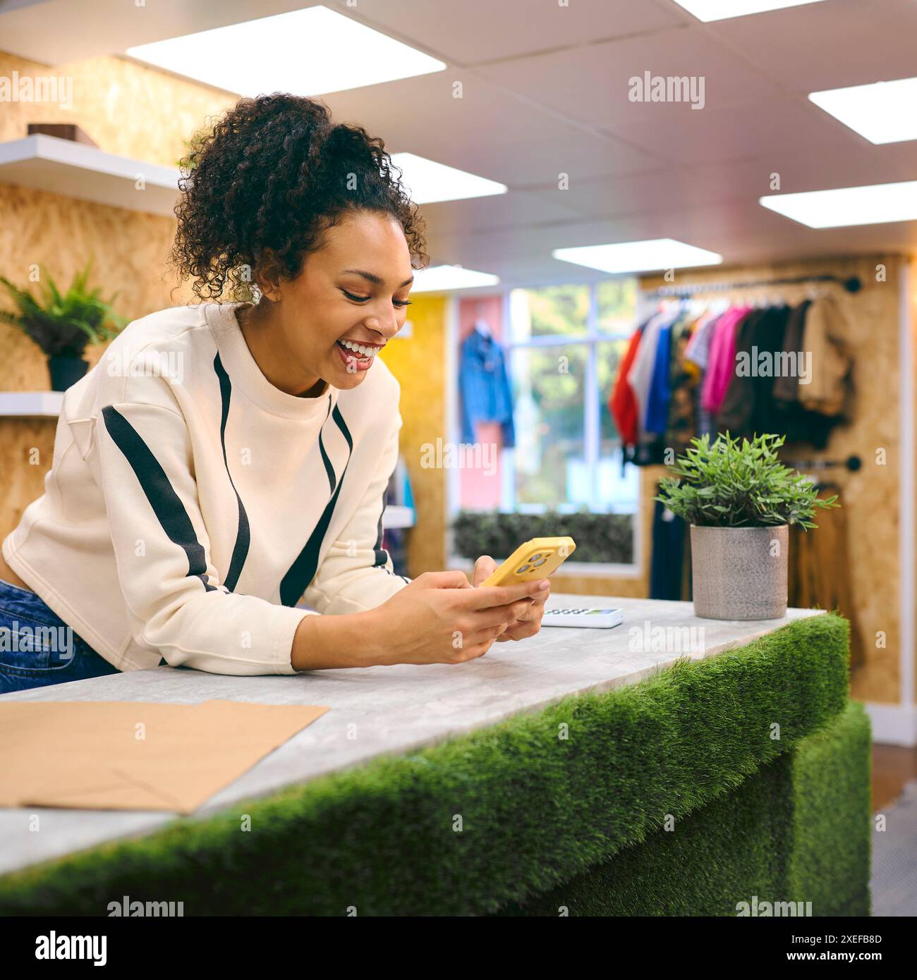 Weibliche Verkäuferin An Der Kasse Im Pop-Up-Mode- Oder Kleidergeschäft, Die Sich Ein Mobiltelefon Anschaut Stockfoto