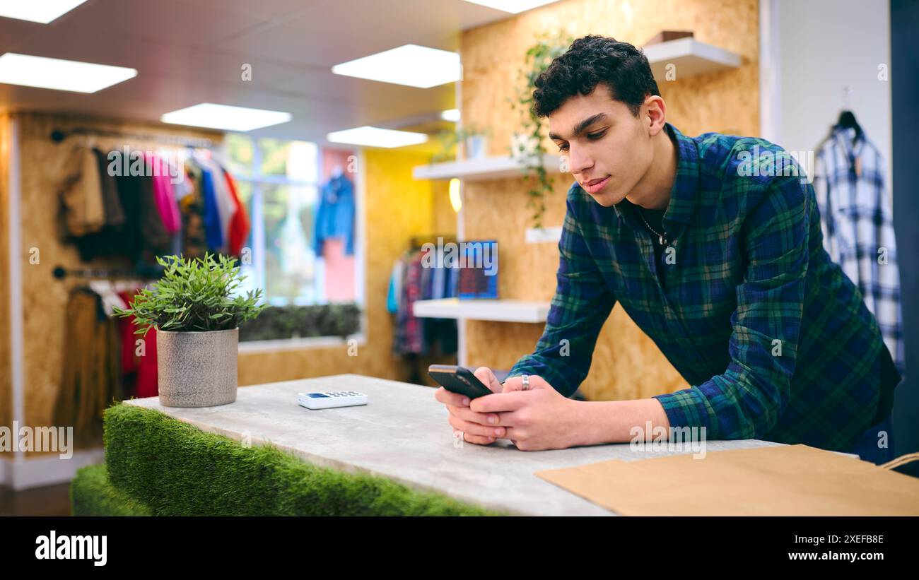 Männlicher Vertriebsmitarbeiter Am Kassenschalter Im Pop-Up-Mode- Oder Kleiderladen, Der Sich Das Mobiltelefon Anschaut Stockfoto