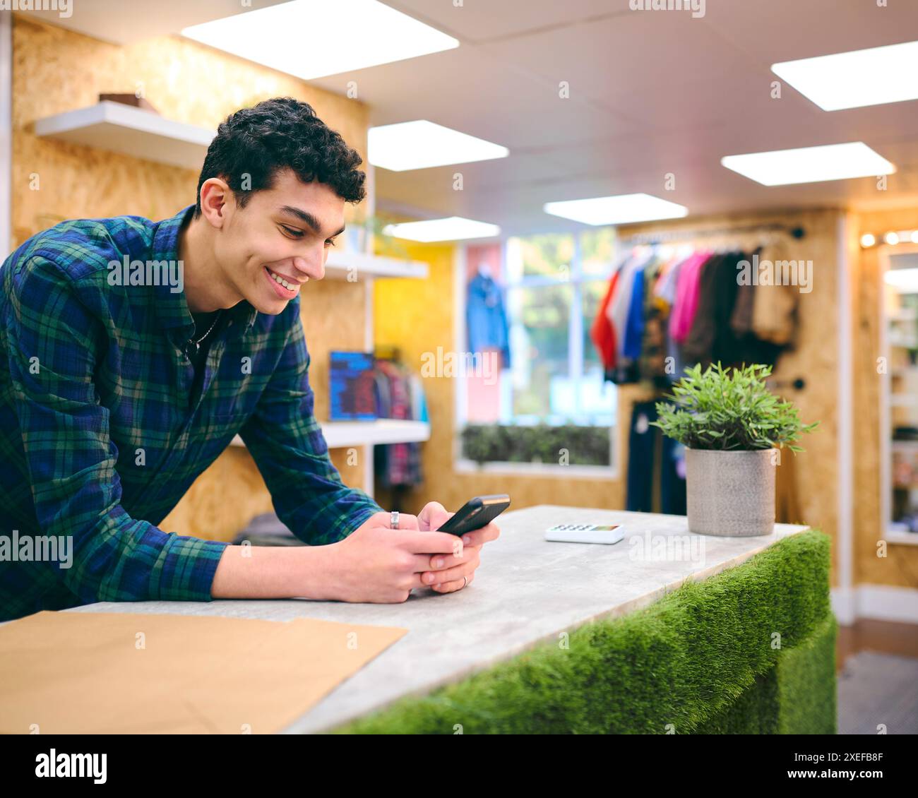 Männlicher Vertriebsmitarbeiter Am Kassenschalter Im Pop-Up-Mode- Oder Kleiderladen, Der Sich Das Mobiltelefon Anschaut Stockfoto