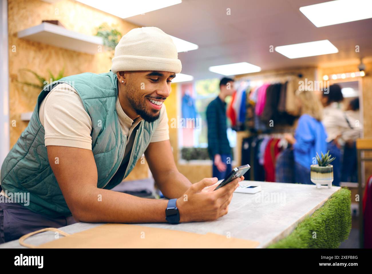 Männlicher Vertriebsmitarbeiter Am Kassenschalter Im Pop-Up-Mode- Oder Kleiderladen, Der Sich Das Mobiltelefon Anschaut Stockfoto