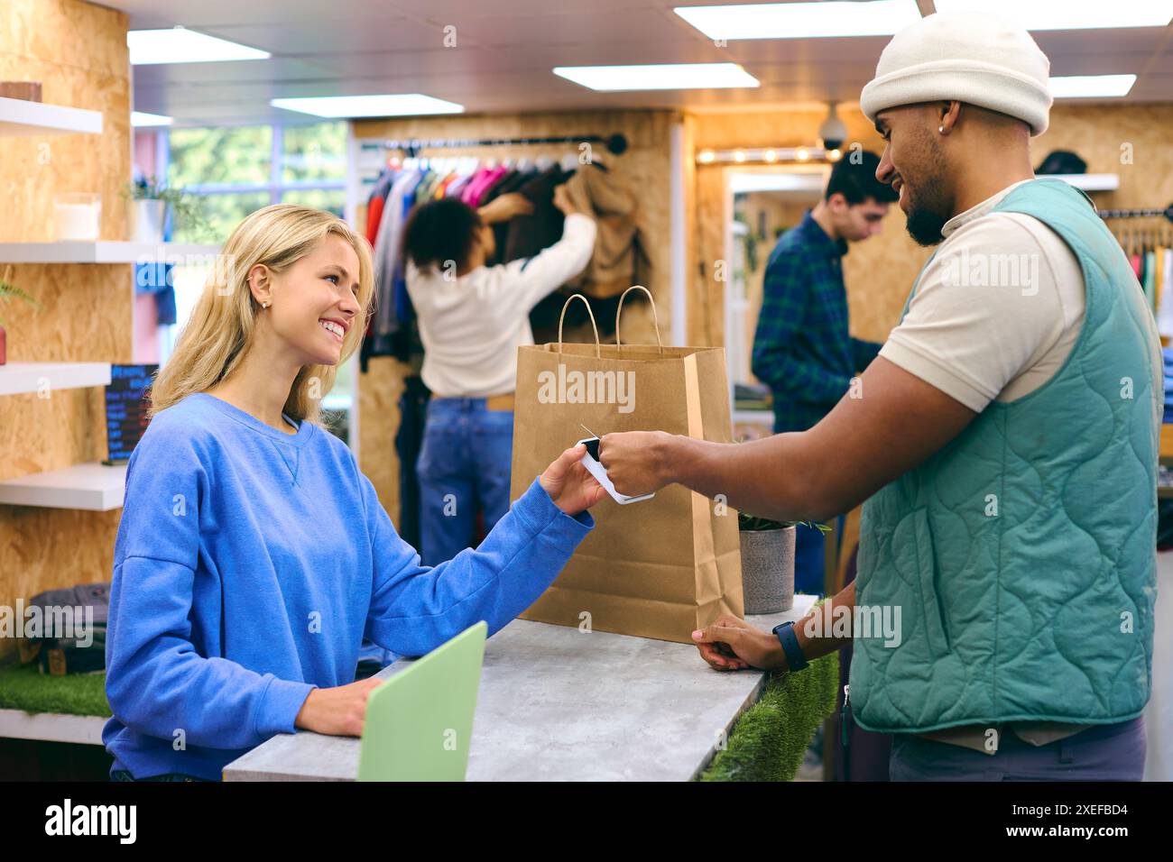Männlicher Kunde Zahlende Weibliche Verkaufsassistentin Im Modegeschäft Mit Kontaktloser Zahlung Mit Karte Stockfoto