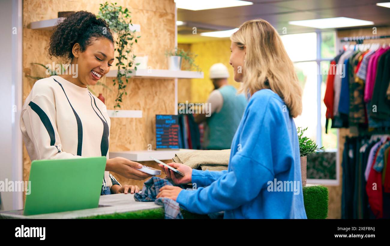 Frau, Die Ein Hemd Von Der Verkäuferin Kauft Und Kontaktlos Mit Dem Mobiltelefon Bezahlt Stockfoto
