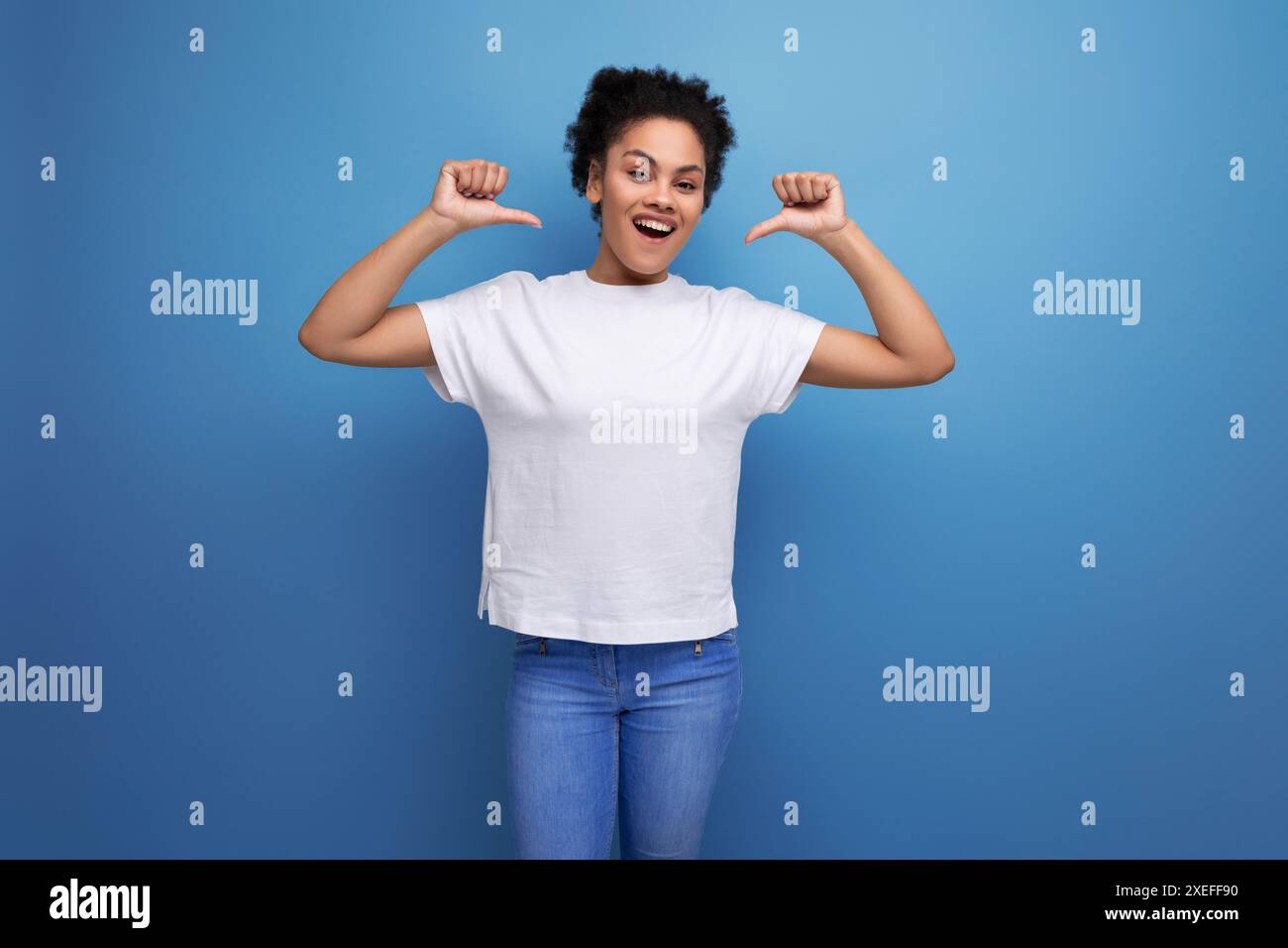 Eine junge brünette Frau mit Afro-Haaren in einem weißen T-Shirt zeigt ihre Hände auf einem leeren Platz für ein Modell Stockfoto