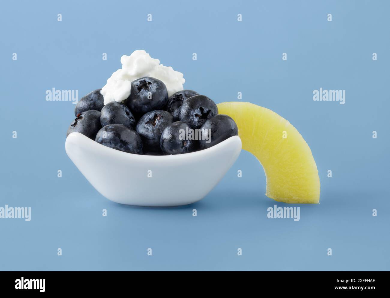 Frische blaue Beeren, garniert mit Hüttenkäse und einer Ananasscheibe in weißer Schale Stockfoto