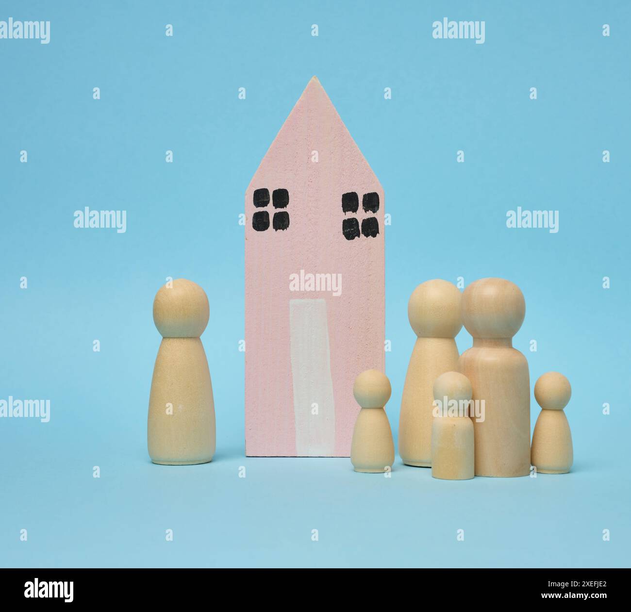 Holzhaus und Miniaturfiguren einer Familie auf blauem Hintergrund. Das Konzept des Verkaufs und Kaufs von Immobilien Stockfoto