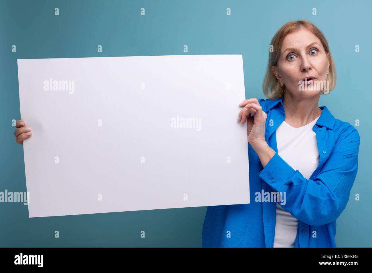 Geschäftskonzept mittleren Alters. Frau mittleren Alters, die ein Poster für Notizen mit einem Mocap auf einem blauen Hintergrund hält Stockfoto