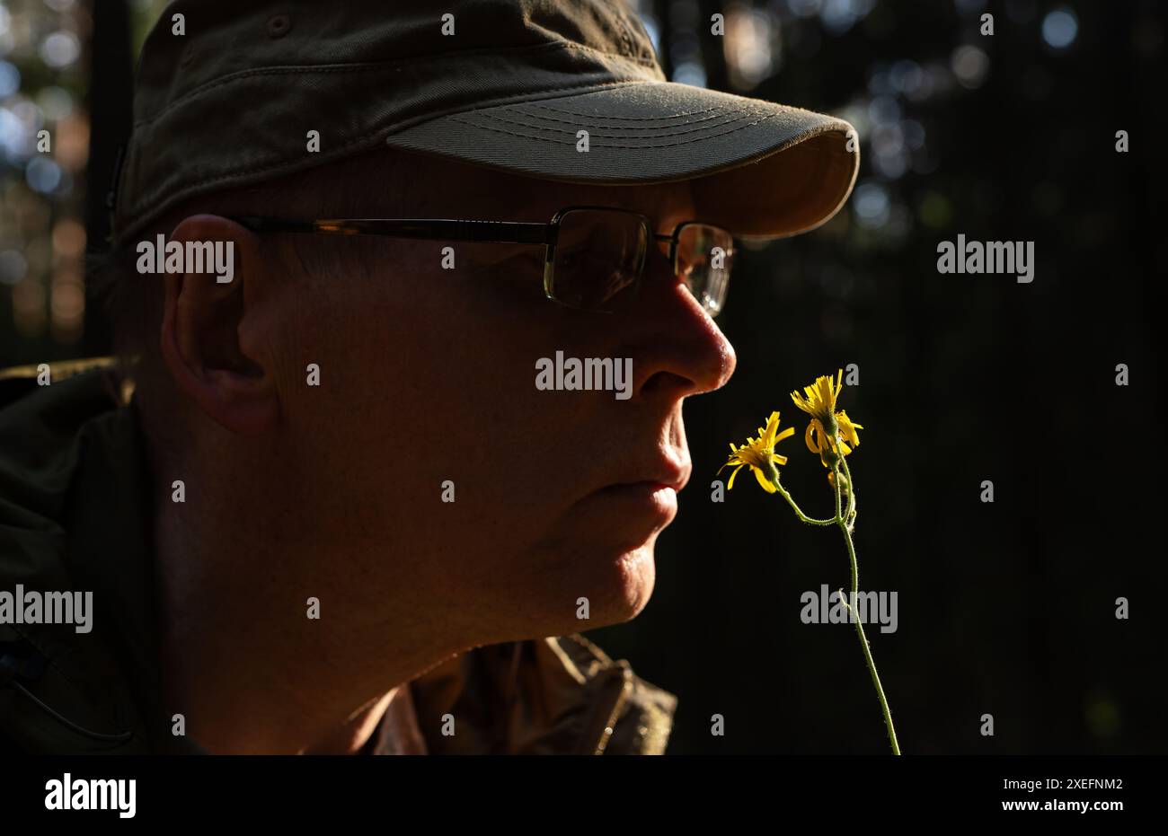 Ein Mann, der Blumen in der Natur genießt. Männliche riechende Blüten, Ruhe und Zen. Porträt im sonnigen Garten. Sommertag, Sonnenlicht und ruhige Schönheit. Einheit mit Stockfoto