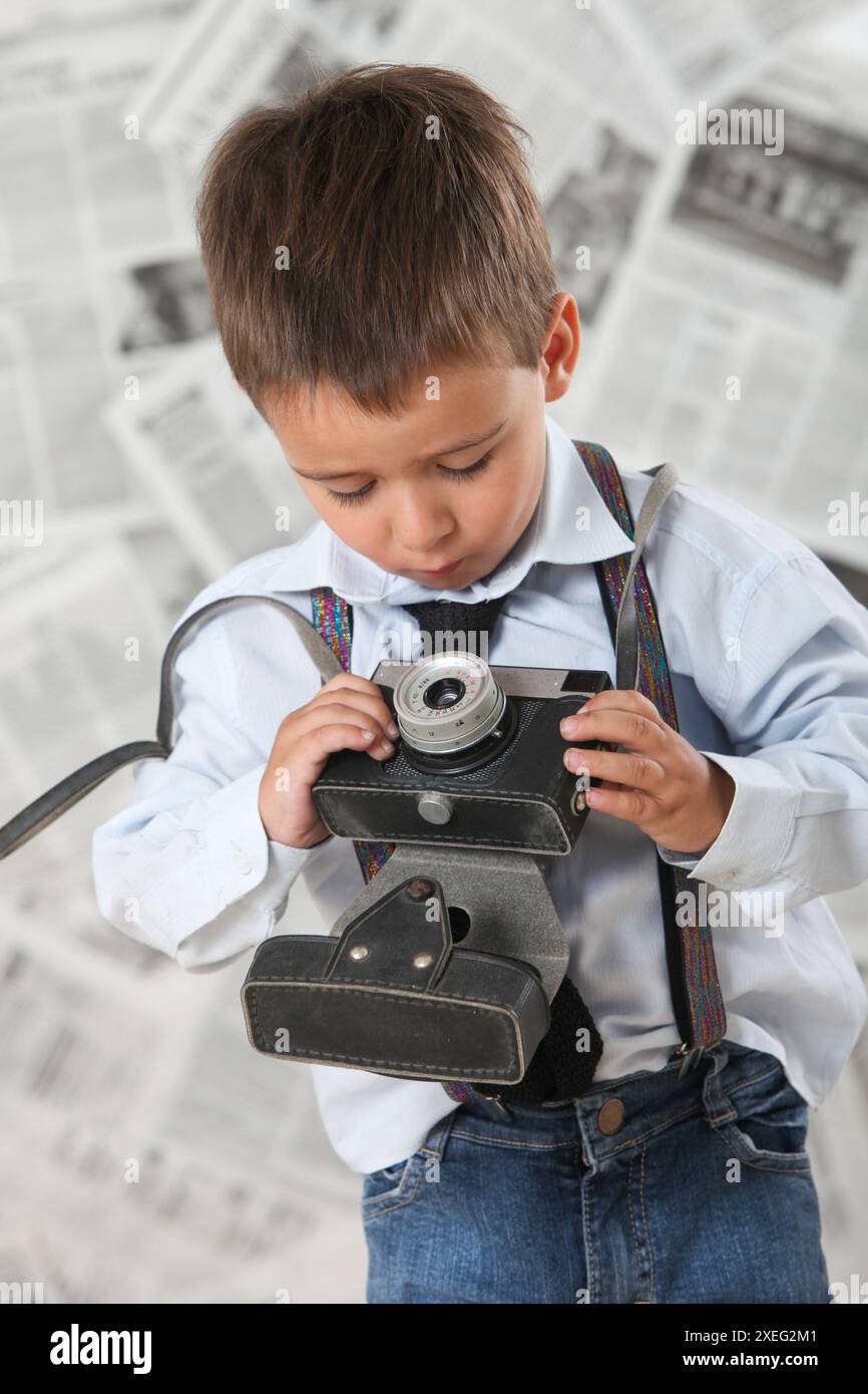 Netter kleiner Junge mit einer alten Fotokamera mit Zeitungen im Hintergrund Stockfoto