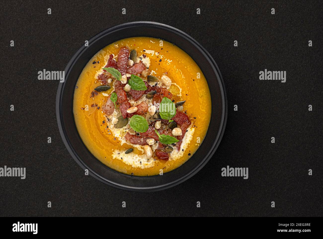 Kürbiscremesuppe mit Kürbiskernen und knusprigem Speck auf schwarzem Hintergrund mit Kopierraum, Draufsicht Stockfoto