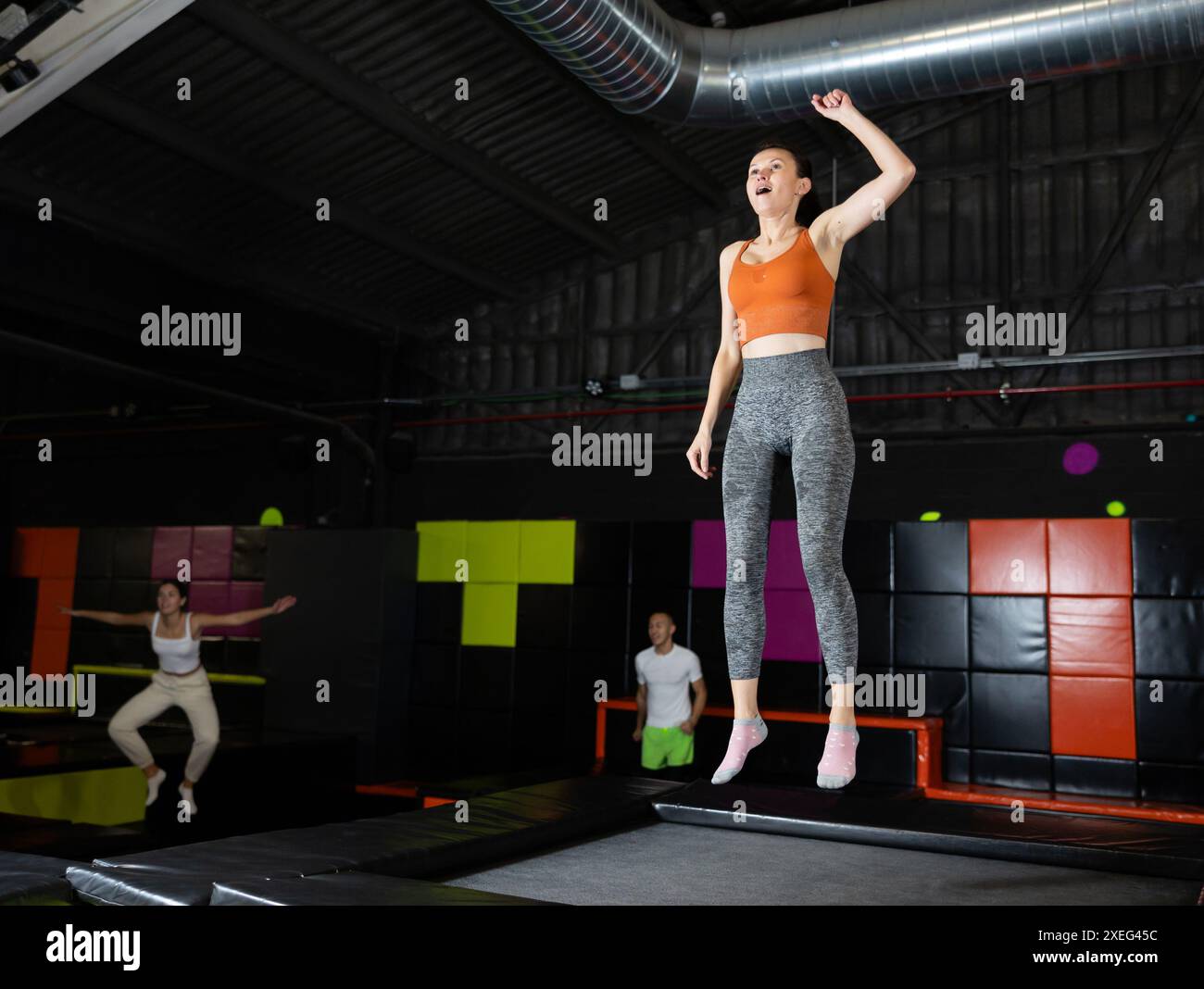 Glückliche Frau mittleren Alters, die auf Trampolinen in einem Sporthalle trampoliniert und springt, Workout und modernes Unterhaltungskonzept Stockfoto