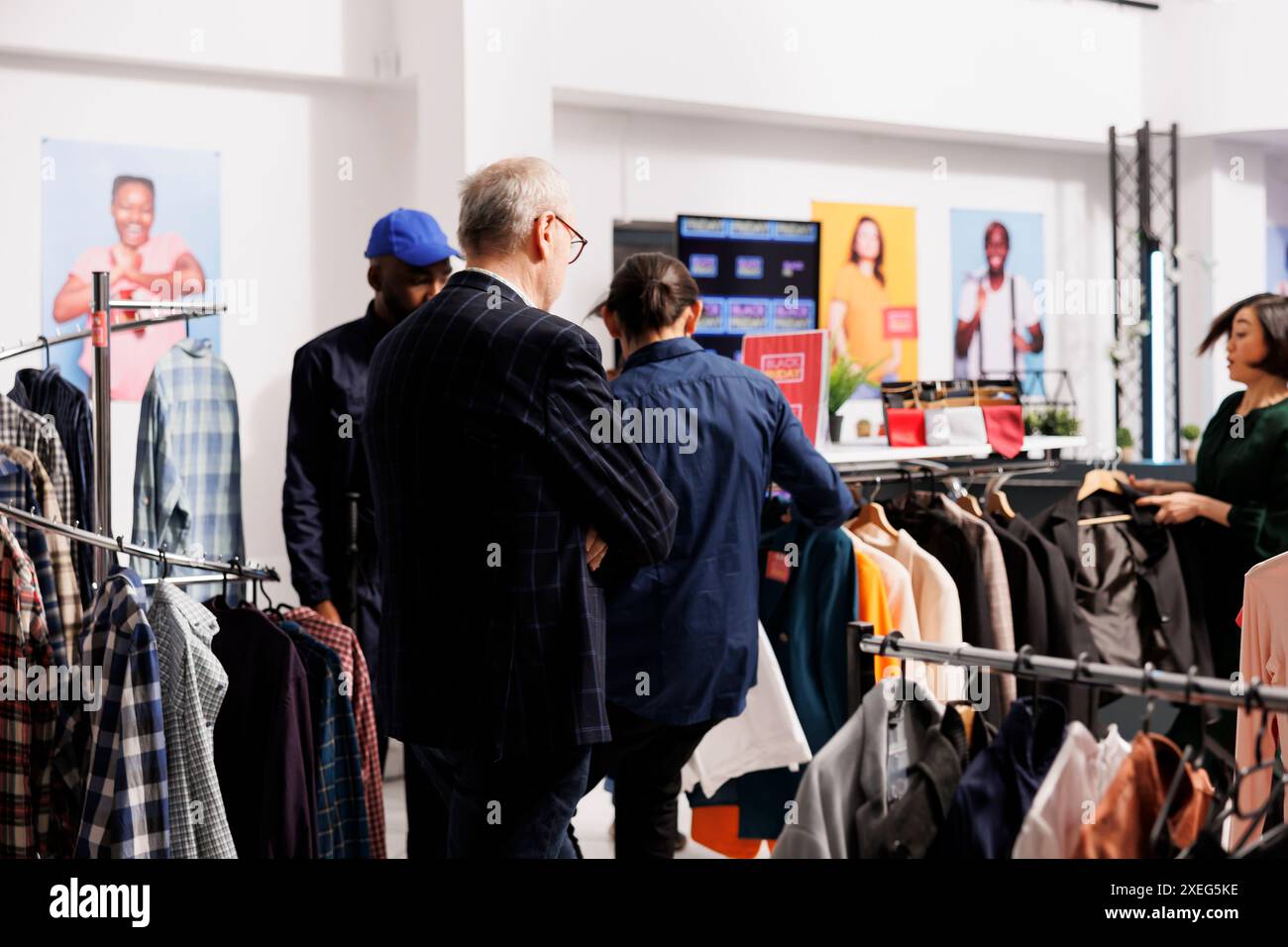 Gruppe von verschiedenen Einkäufern, die im Bekleidungsgeschäft stehen und Kleidung zu ermäßigten Preisen auswählen. Kunden, die bei den Black Friday-Angeboten verrückt werden, suchen nach Schnäppchen bei saisonalen Moderabatten Stockfoto