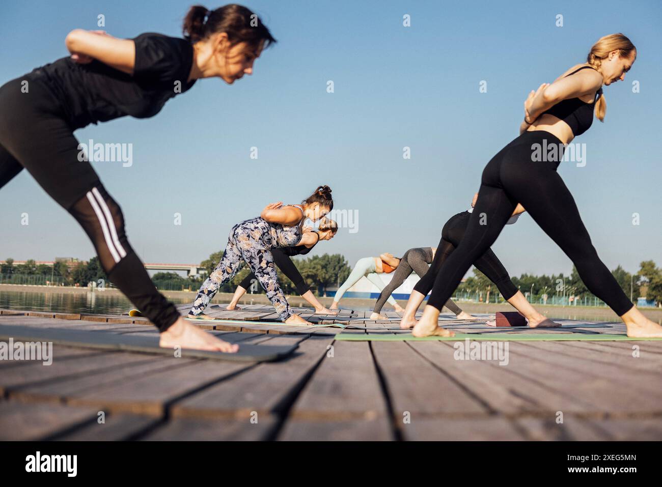 Yoga-Kurs mit einem Lehrer am Yachthafen in der Stadt. Junge Frauen stehen mit den Händen in Namaste-Geste auf den Matten und d Stockfoto