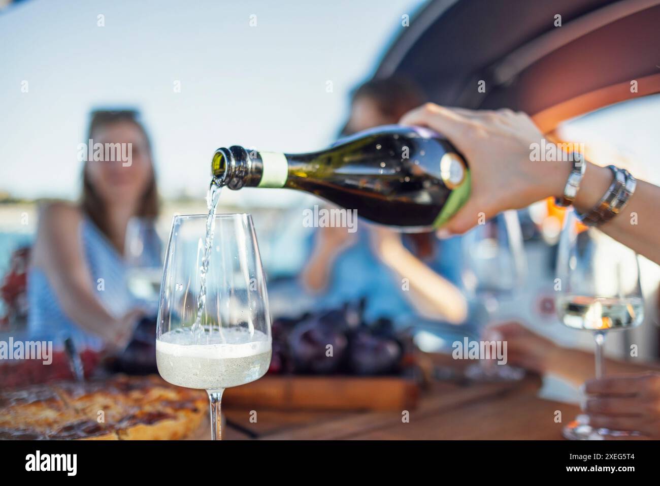 Ein lächelndes Mädchen in der Sonnenbrille gießt Champagner in Gläser. Mittagessen während der Bootstour auf dem Meer. Stockfoto