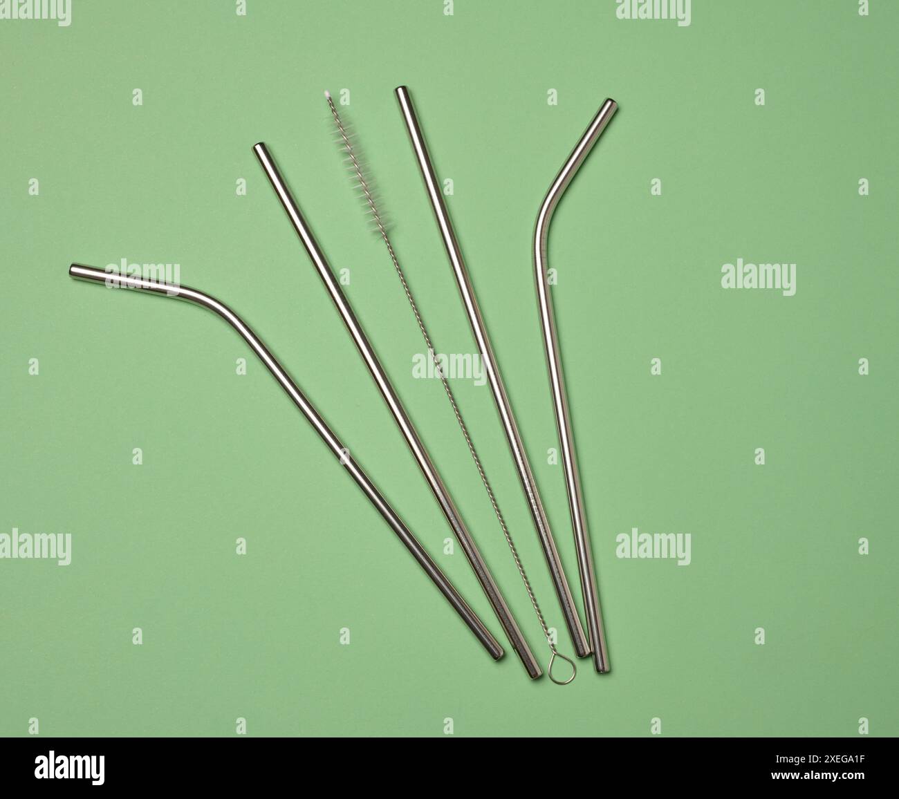 Metallhalme für Cocktails und eine Reinigungsbürste auf grünem Hintergrund Stockfoto