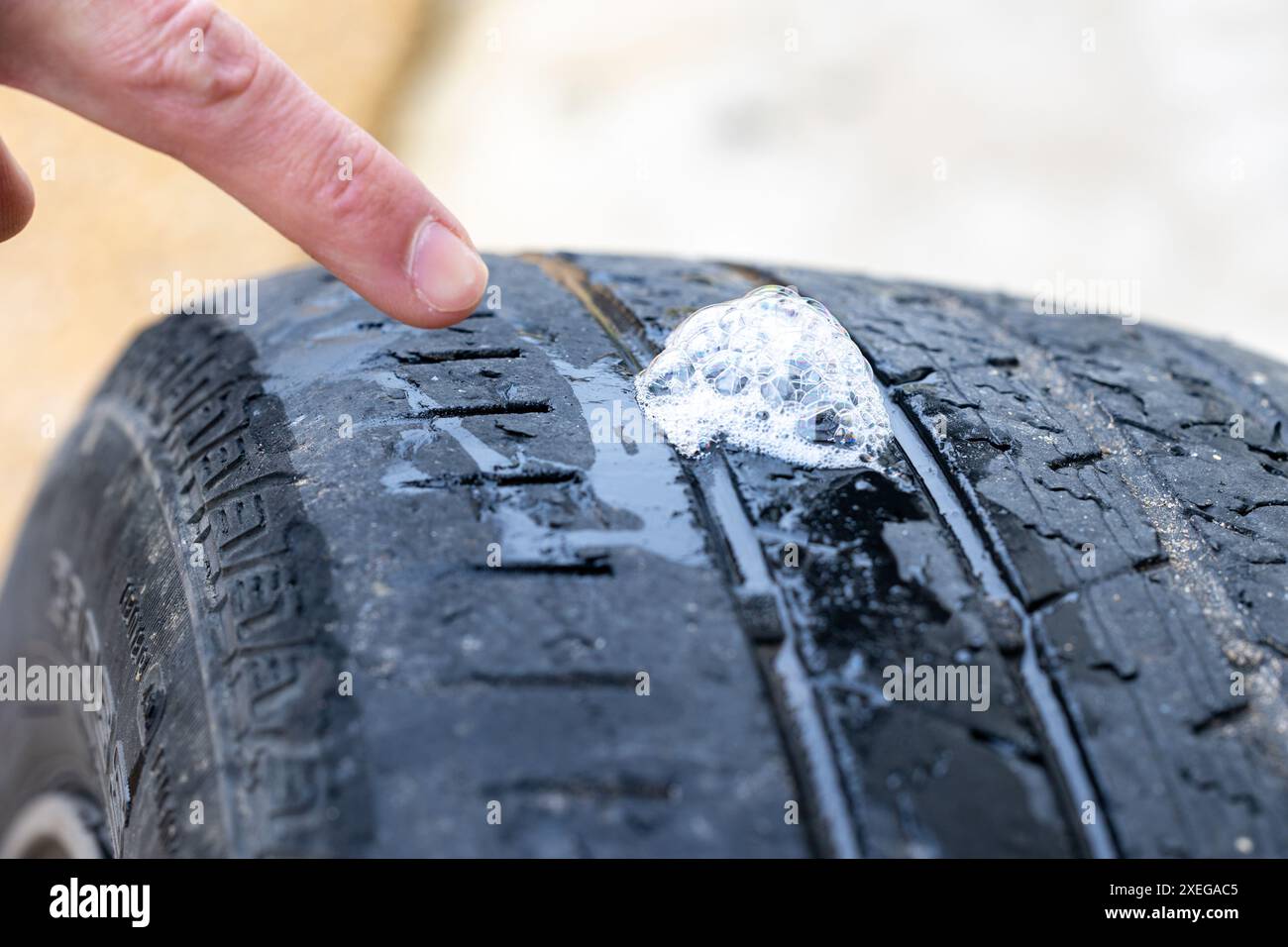 Der Finger zeigt auf Seifenblasen am Reifen, um das Loch zu lokalisieren Stockfoto