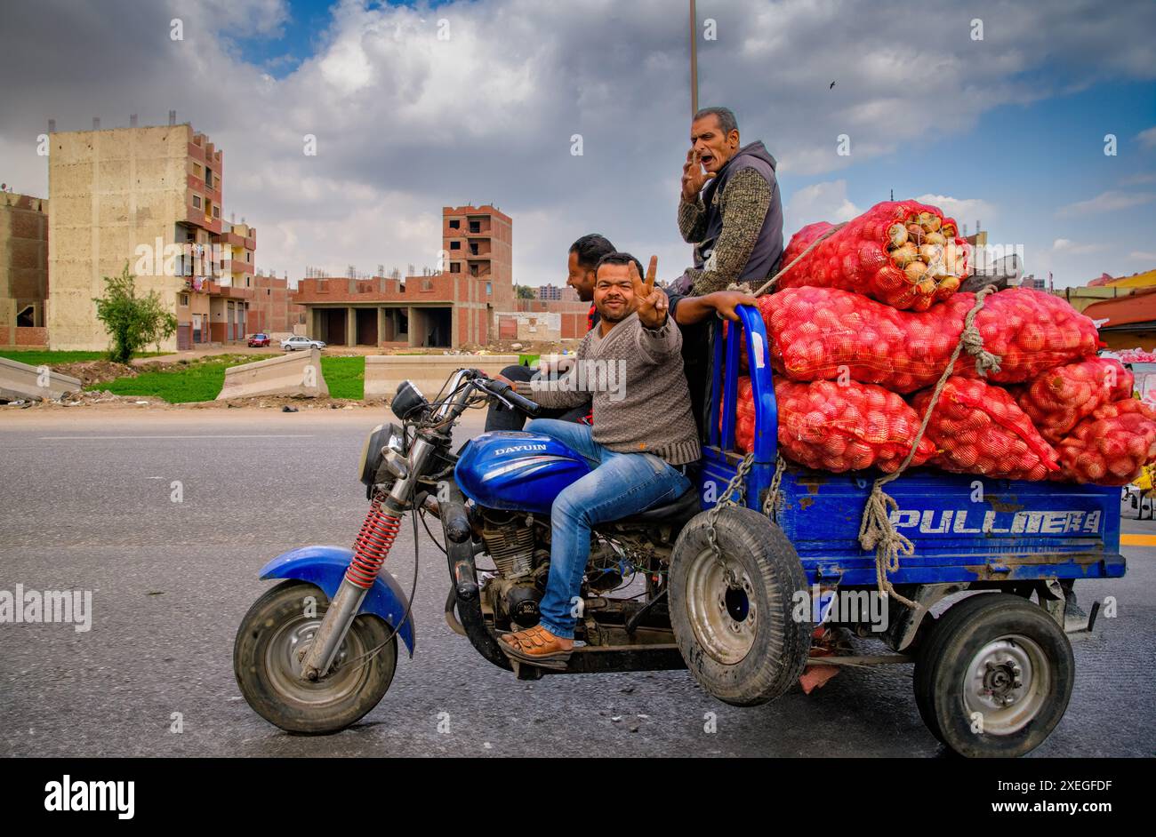 3 ägyptische Männer, die in Kairo auf einem motorisierten Lastdreirad fahren und eine Ladung Zwiebeln transportieren Stockfoto