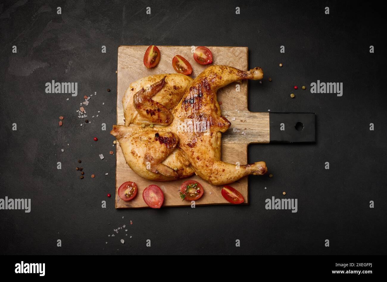 Ganze gebratene Hühnchen mit Gewürzen auf einem Holzbrett auf einem schwarzen Tisch Stockfoto
