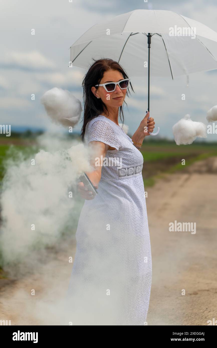 Hübsche Frau in einem weißen Kleid und süßen Wolken mit Rauch und einem Regenschirm Stockfoto