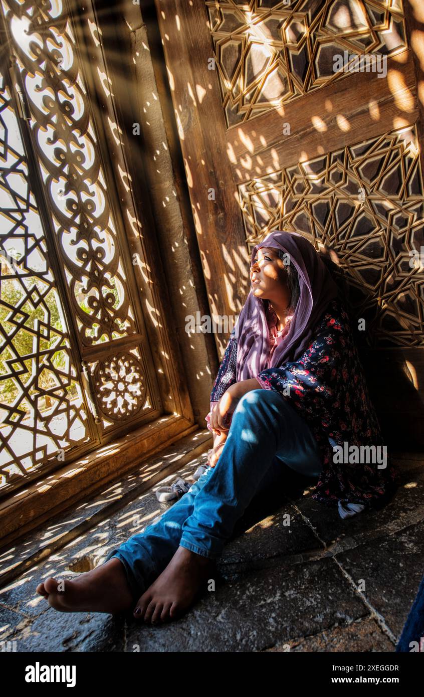 Amira wird von den Sonnenstrahlen beleuchtet, die durch die dekorativen Gitterfenster in der Al-Rifai Moschee leuchten Stockfoto