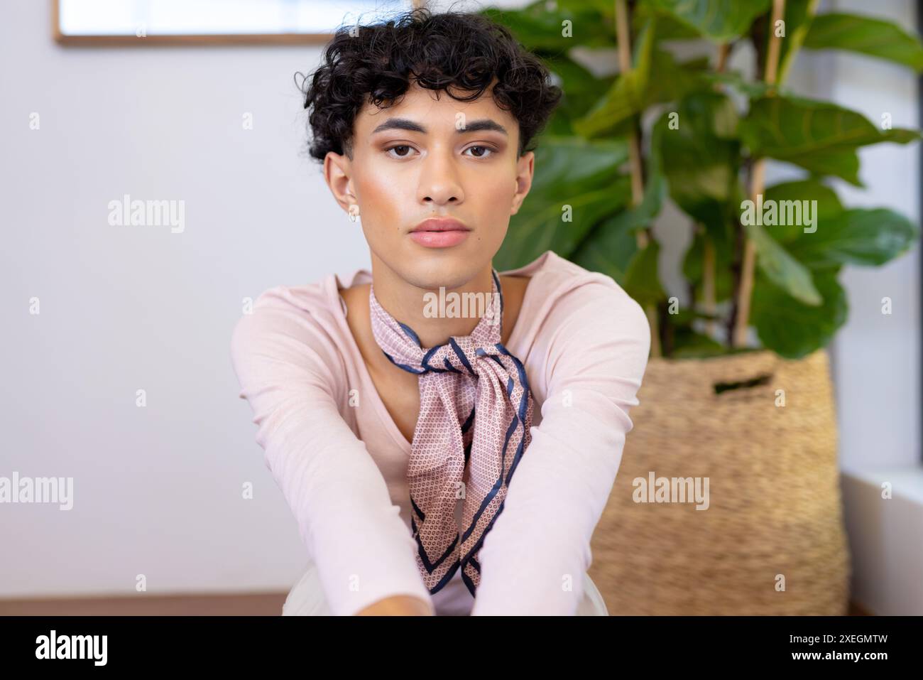 Drinnen sitzt eine Transgender-Transgender-Frau, die selbstbewusst mit Pflanzen im Hintergrund posiert Stockfoto