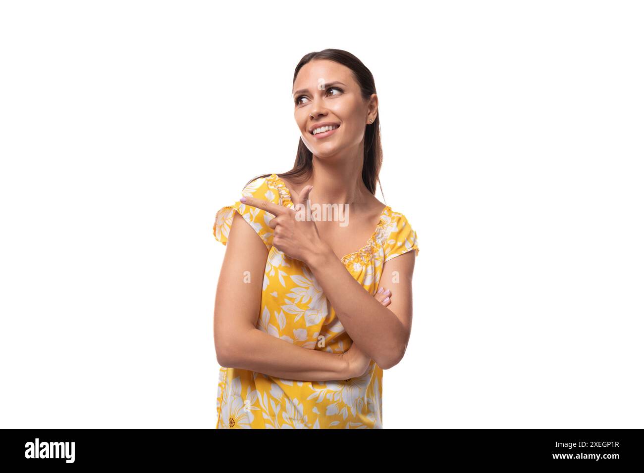 Eine junge Frau mit geradem schwarzem Haar in einem gelben Sommerkleid mit einem Druckmuster lächelt auf weißem Hintergrund Stockfoto