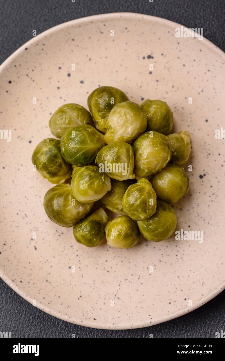 Köstliche gekochte Rosenkohl auf einer Keramikplatte auf dunklem Betonhintergrund Stockfoto