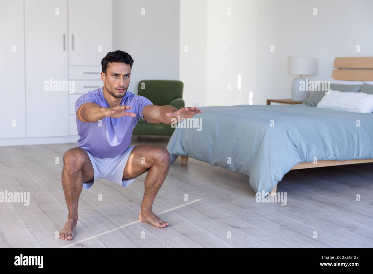 Zu Hause trainieren, Mann, der Squats im Schlafzimmer macht, um Fitness-Routine zu machen Stockfoto