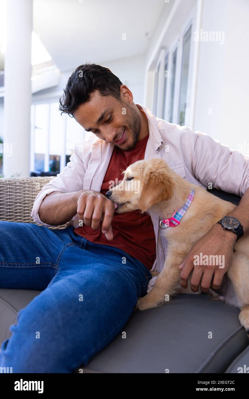 Er spielt mit dem Welpen, der Mann sitzt auf der Couch und genießt zu Hause eine gute Zeit Stockfoto