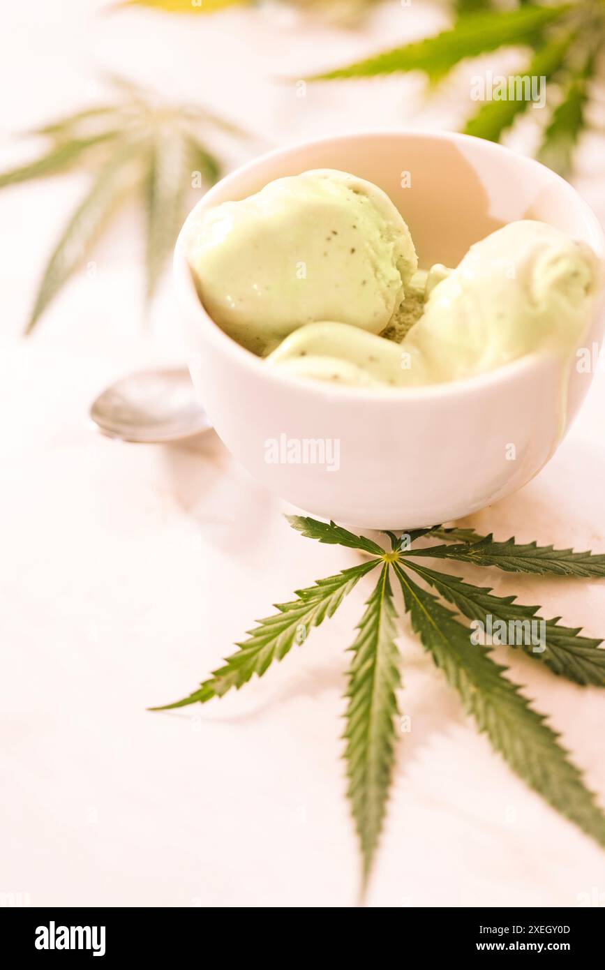 Ein Hanfblatt liegt auf einem nachgeahmten Glas Eis auf einem weißen Marmortisch Stockfoto