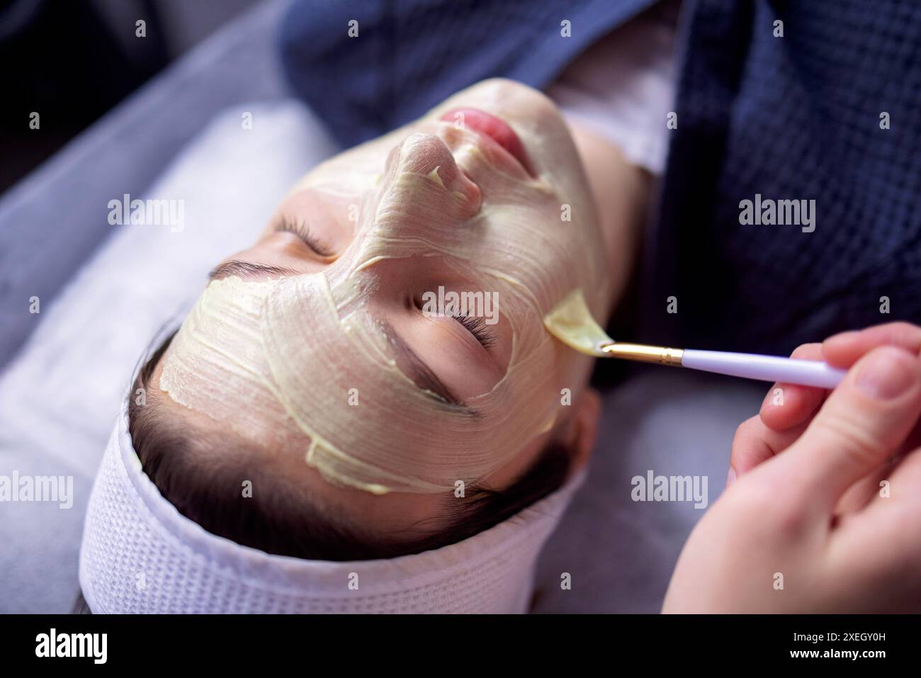 Der Schönheitsmeister wendet eine verjüngende Maske auf das Gesicht des Kunden an Stockfoto